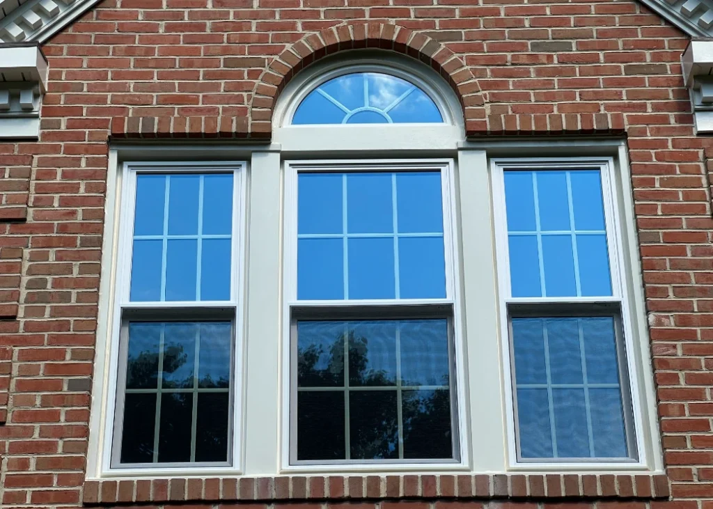 a red brick building with two windows and a clock. - Clifton Exteriors, LLC Window with arch